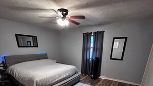 A bedroom with a bed, a ceiling fan, a nightstand, a mirror, and a window with curtains. - Roomy 4-bed house in Springfield + Pet friendly + Gym + Workspace (Springfield)
