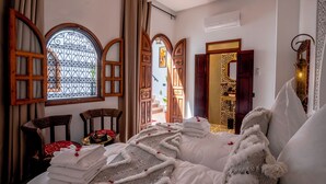 Une pièce comprenant un lit, deux chaises, une fenêtre avec des rideaux et une porte dotée d’un miroir.