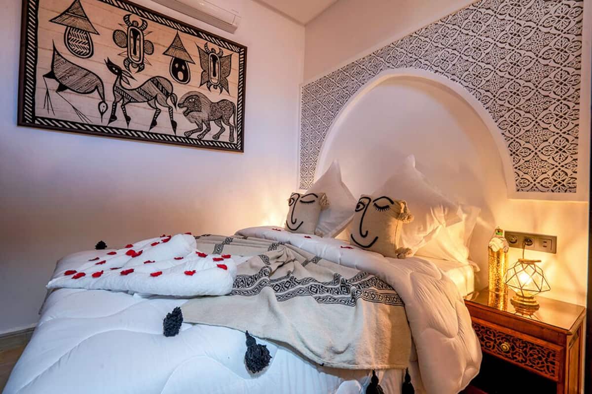A bed with a white headboard, a patterned blanket, and a wall with a geometric design.