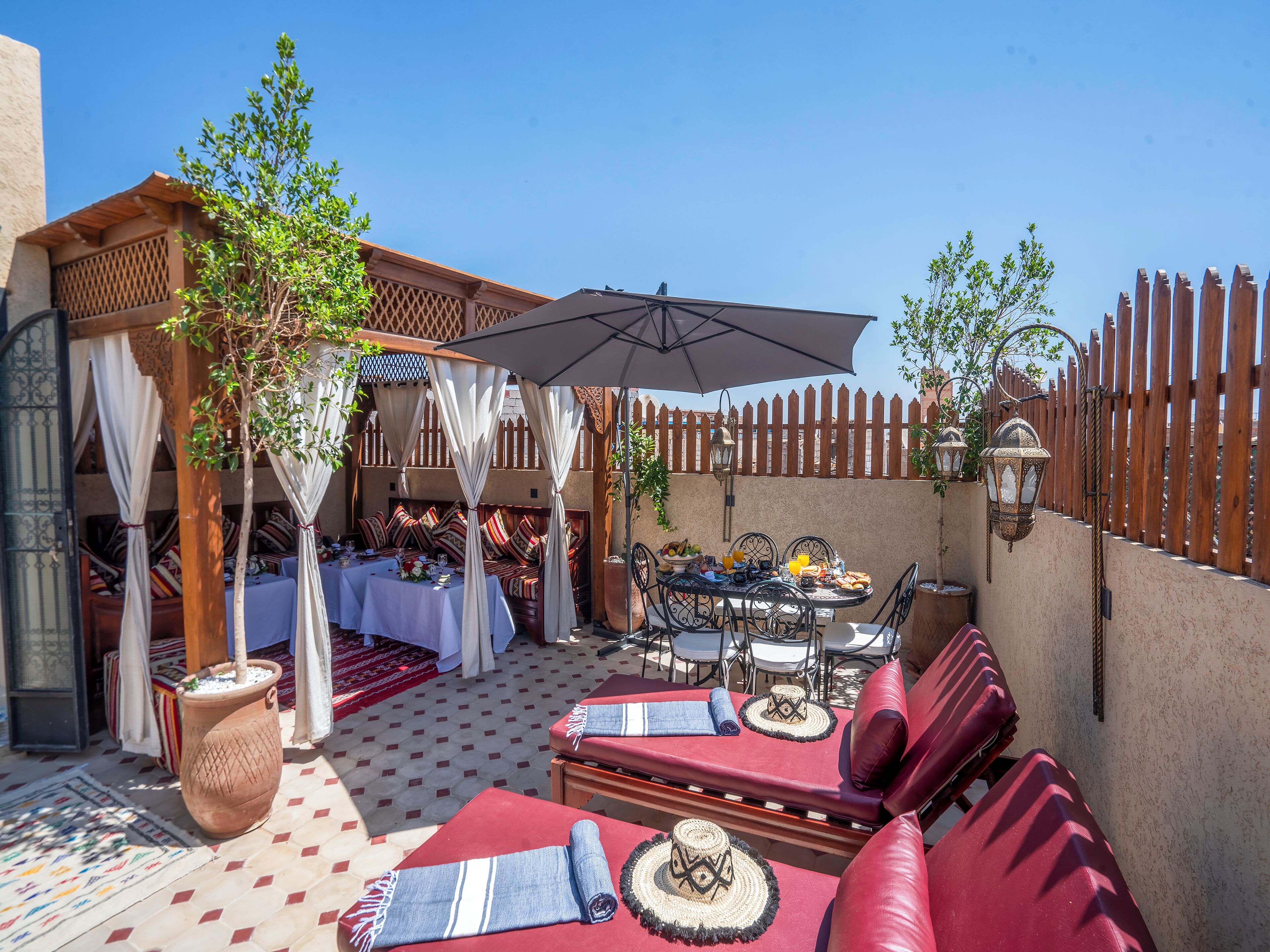 A patio with a table set for dining, cushioned seating, and a pergola with draped fabric.