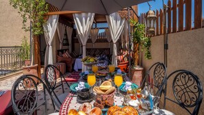 Un espace de restauration en plein air avec une table dressée pour le petit-déjeuner, comprenant du pain, des viennoiseries et des fruits.