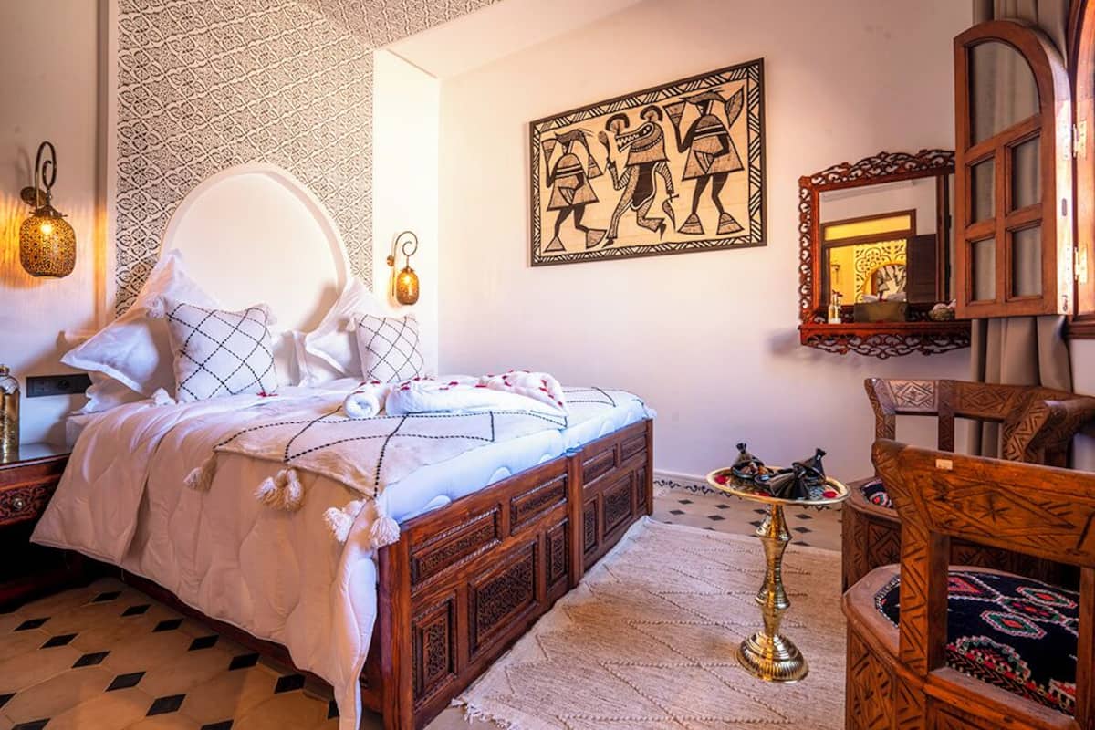 A bedroom with a large bed, a wooden chair, a patterned wall, and a decorative mirror.