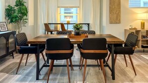 Un coin repas avec une table en bois et des chaises noires, une plante en pot et une fenêtre avec des rideaux.