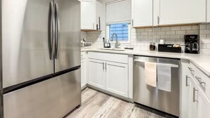 Une cuisine moderne avec des meubles blancs, des appareils en acier inoxydable et une fenêtre équipée de stores.