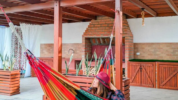 Een hangmat onder een houten pergola met een stenen openhaard en houten kasten.