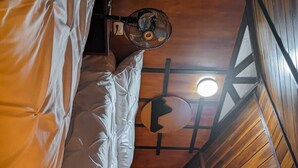Een smalle kamer met houten lambrisering, twee bedden, een plafondventilator en een dakraam.