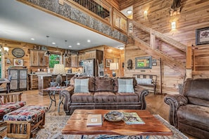 A spacious living area with a high ceiling, wooden walls, a staircase, and a kitchen in the background. - Rustic 3bed Cabin w/ Perfect Views of The Smokies! (Gatlinburg)