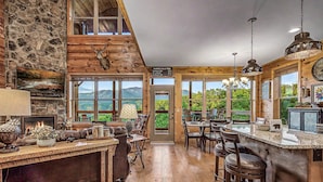 A rustic interior with a stone fireplace, wooden ceiling, and a view of mountains through large windows. - Rustic 3bed Cabin w/ Perfect Views of The Smokies! (Gatlinburg)