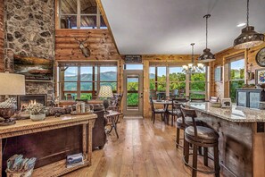 Un intérieur rustique avec une cheminée en pierre, un plafond en bois et une vue sur les montagnes grâce à de grandes fenêtres.