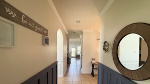 A hallway with a sign reading "be our guest," a round mirror, and a view into a room with a chair and a table. - Charming 3-bedroom house in Lake Conroe, community pool and gym. (Montgomery)