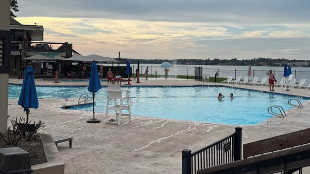 A swimming pool with lounge chairs and umbrellas, a view of the water, and a building in the background. - Charming 3-bedroom house in Lake Conroe, community pool and gym. (Montgomery)