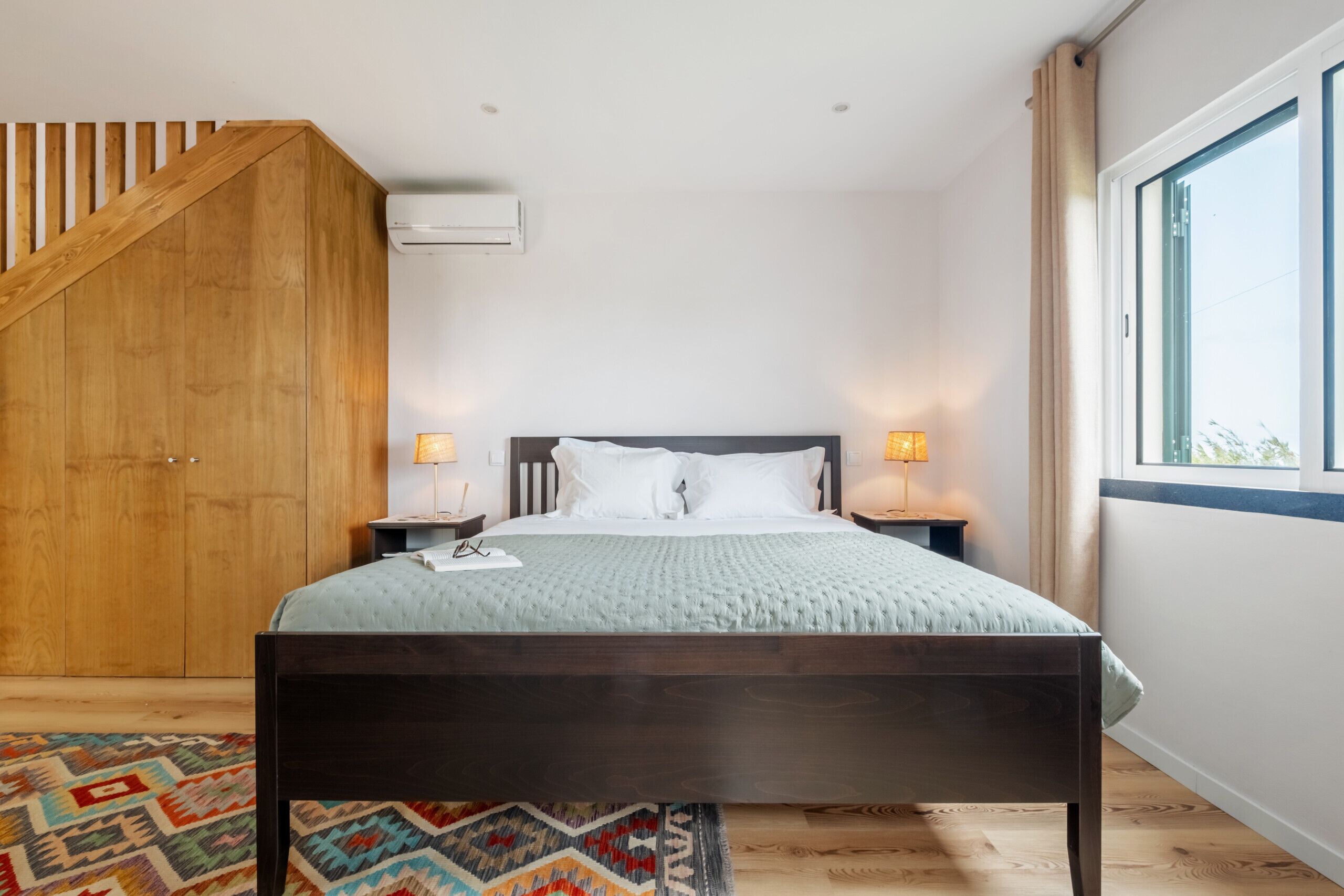 A bedroom with a bed, nightstands, a window, and a wooden staircase.