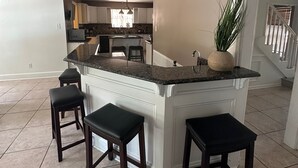 Una cocina amplia con una isla central, taburetes de bar y una planta en maceta.