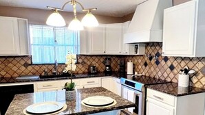 Una cocina moderna con armarios blancos, encimera de granito, una isla central con taburetes e iluminación colgante.