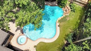 Una piscina con un hidromasaje circular, rodeada de césped cuidado y árboles.