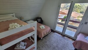 Un dormitorio con dos camas, una puerta corrediza de vidrio al exterior y una pequeña mesa con una silla.