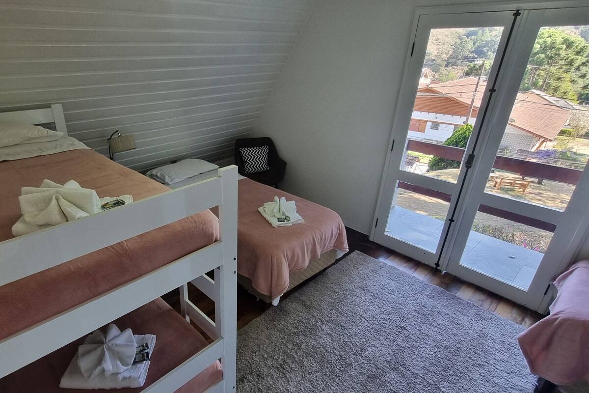 Un dormitorio con dos camas, una puerta corrediza de vidrio al exterior y una pequeña mesa con una silla.