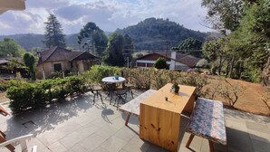 Un patio con una mesa y sillas de madera, rodeado de vegetación y casas al fondo.