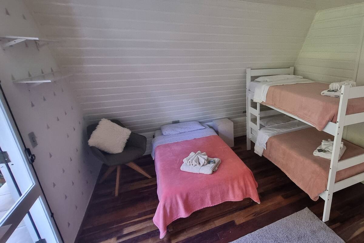 Habitación con literas, una colcha rosa, una pequeña silla y un armario blanco.