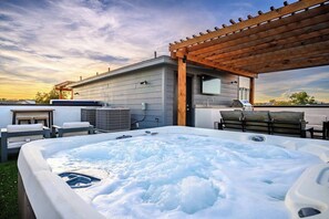 Ein Whirlpool umgeben von Gartenmöbeln, einer Pergola und Klimaanlagen auf einem Dach.