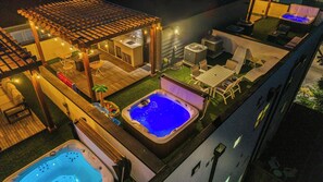 Eine Dachterrasse mit Whirlpool, Sitzgelegenheiten im Freien und einer Pergola mit Lichterketten.