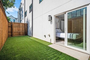 A modern building with a well-maintained lawn, a wooden fence, and a glass door leading to a bedroom.