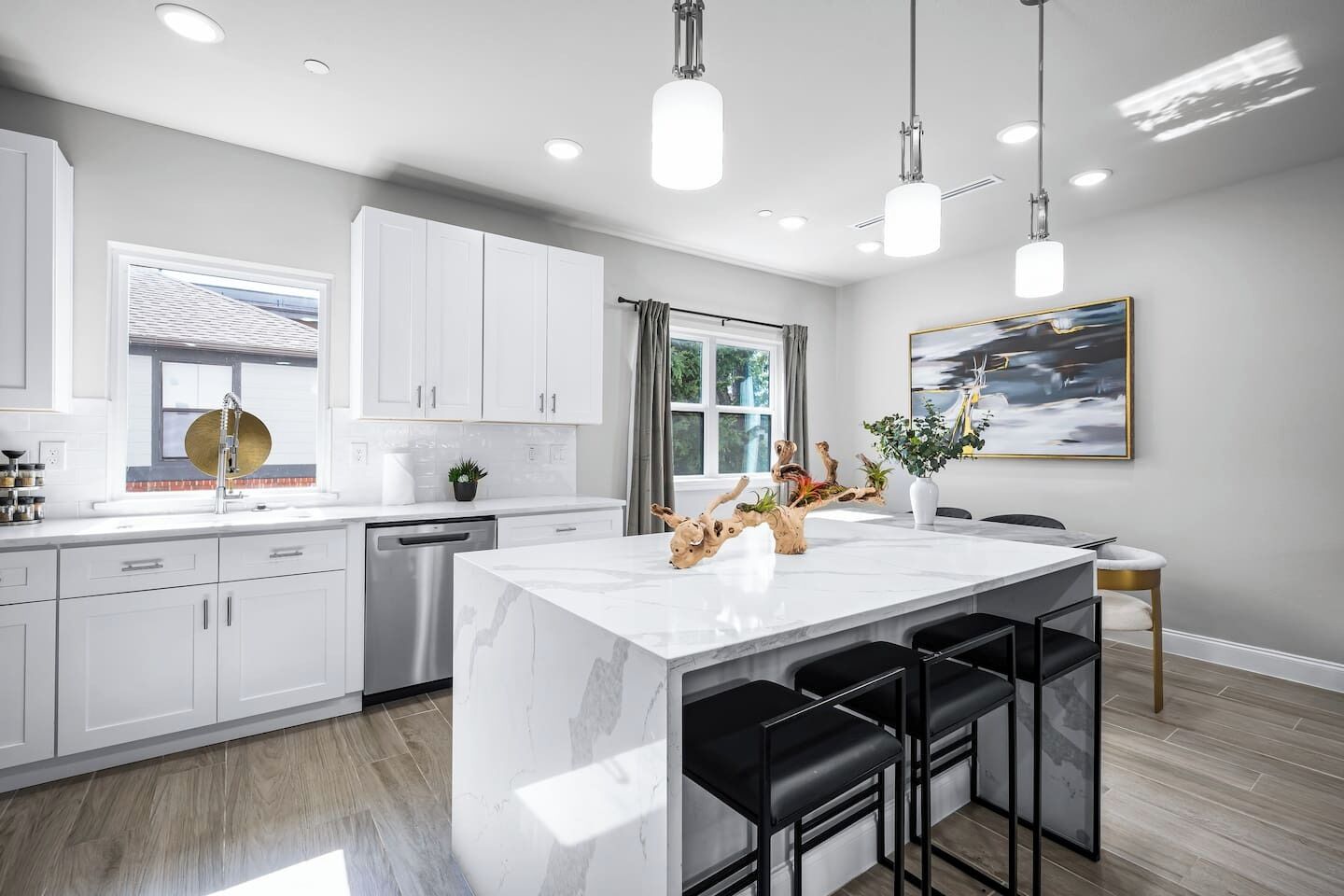 A modern kitchen with white cabinets, a marble island, black bar stools, and pendant lighting.