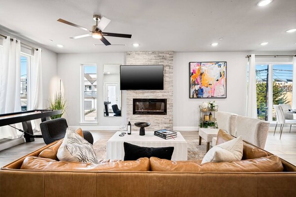 A modern living room with a leather sofa, a flat-screen TV, a fireplace, and a dining area with a view.