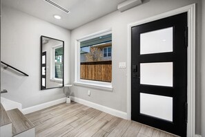 A hallway with a black door, a window with a view of a wooden fence, and a mirror on the wall.