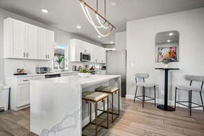 A modern kitchen with white cabinets, a marble island, and a dining area with two bar stools.