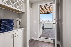 A room with a white door leading to an outdoor patio with a pergola, a stack of towels, and a fan on a shelf.
