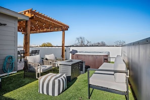 A backyard patio with a pergola, outdoor furniture, a hot tub, and a well-maintained lawn.