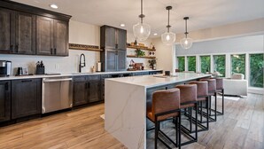 Una cocina moderna con una isla de mármol, armarios de madera oscura e iluminación colgante.