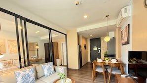 A modern living room with a sofa, a small round table with a plant, and a dining area with a wooden table and chairs. - The Deck Patong Phuket by Mickey (Patong)
