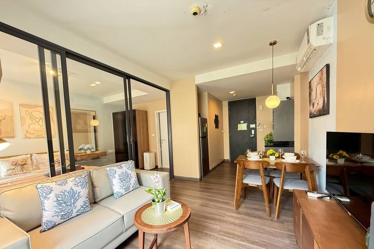 A modern living room with a sofa, a small round table with a plant, and a dining area with a wooden table and chairs.