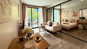 A spacious living room with a sofa, a dining table with a vase of flowers, and a large sliding glass door leading to a balcony. - The Deck Patong Phuket by Mickey (Patong)