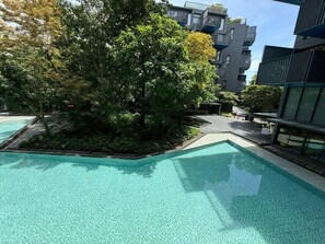 A modern building with a swimming pool surrounded by lush greenery and trees. - The Deck Patong Phuket by Mickey (Patong)