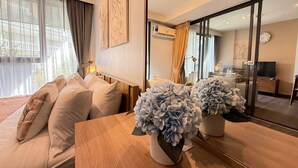 A modern hotel room with a large bed, a wooden nightstand, a vase of flowers, and a large mirror reflecting the room. - The Deck Patong Phuket by Mickey (Patong)