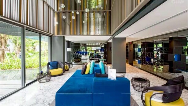 A modern interior with a blue sectional sofa, yellow chairs, and a glass wall providing a view of the outdoors. - The Deck Patong Phuket by Mickey (Patong)