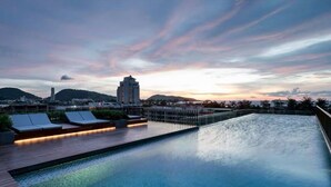 A rooftop pool with lounge chairs and a view of a cityscape at sunset. - The Deck Patong Phuket by Mickey (Patong)