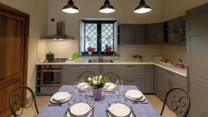 Een moderne keuken met grijze kastjes, een ingebouwde oven en een eethoek voor zes personen met een paarse tafelkleed.