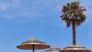 A poolside area with lounge chairs and thatched umbrellas, palm trees, and a clear blue sky. - Spacious Studio at Estrela Da Luz, pools, indoor spa and gym. (Luz)