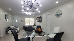 A modern dining area with a glass table and black and white chairs, a ceiling light fixture, and a clock on the wall. - Tranquil 2-bedroom house with AC in Spring Hill (Spring Hill)