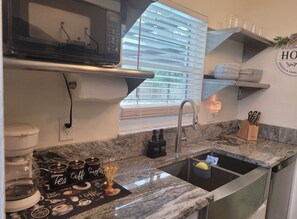 Eine Küche mit einer Arbeitsplatte aus Granit, einer Kaffeemaschine und einem Spülbecken. Über der Arbeitsplatte befinden sich Regale mit Tellern und Gläsern.