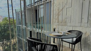 A balcony with a table set for two, chairs, and a view of a building and trees. - Luxury Studio Private pool IIK C409SF (Tulum)