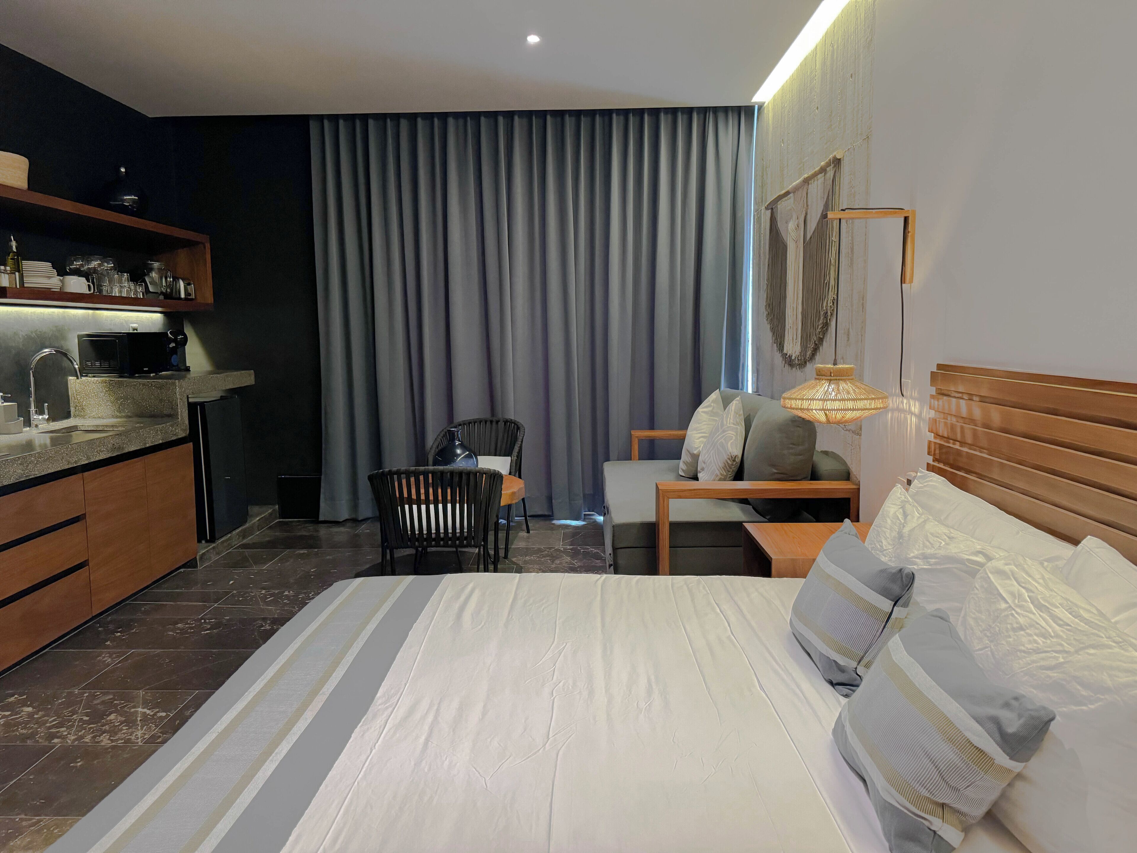Une chambre d’hôtel comprenant un lit, un bureau, une chaise, un canapé, un coin repas avec un four à micro-ondes et une grande fenêtre avec des rideaux.