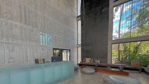 A modern reception area with a concrete wall, a reception desk, and a seating area with a sofa and ottomans. - Luxury Studio Private pool IIK C409SF (Tulum)
