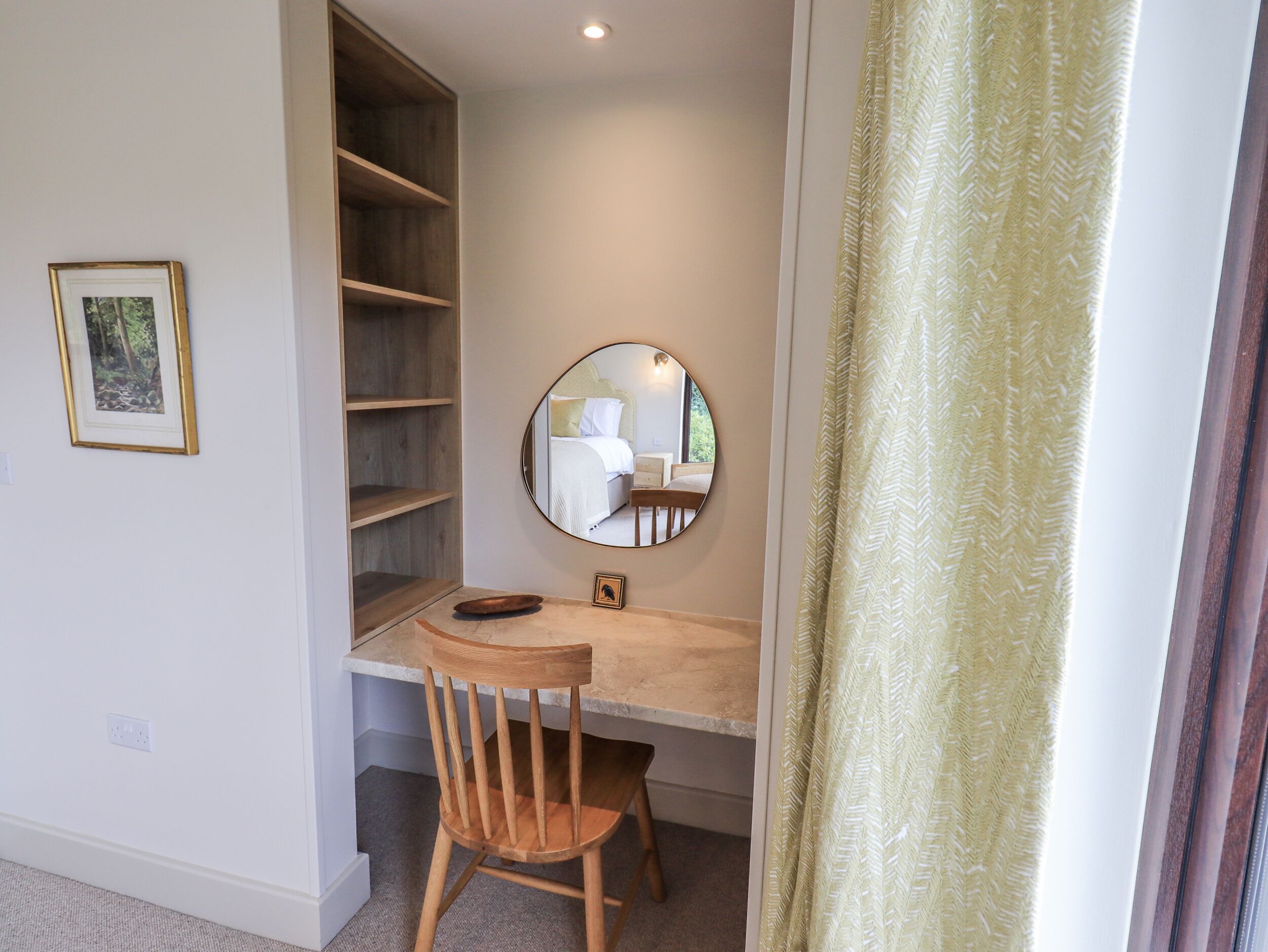 A room with a desk, a chair, a mirror, a bookshelf, and a window with curtains.