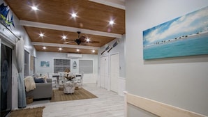 A spacious living area with a wooden ceiling, a dining table with chairs, and a painting of birds on the wall.
