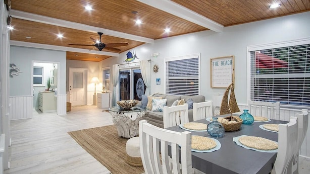 A dining area with a wooden ceiling, white walls, and a view of the beach through the window.